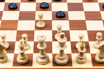 playing by different rules on the same board - black checkers and white chess figures on wooden chessboard, white pawns attack black checkers (focus on front pawn)