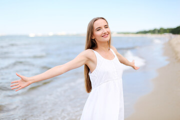 Fototapeta na wymiar Happy smiling woman in free happiness bliss on ocean beach standing with open hands. Portrait of a multicultural female model in white summer dress enjoying nature 
