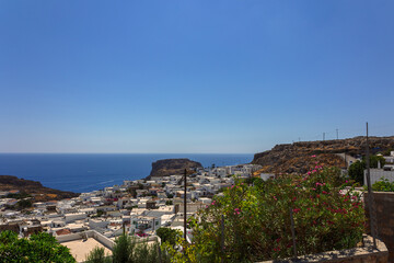 Panoramic view of colorful harbor in Lindos village and Acropolis, Rhodes. Aerial view of beautiful landscape, ancient ruins, sea with sailboats and coastline of island of Rhodes in Aegean Sea