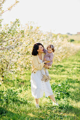 Obraz premium happy mother and daughter on a walk in a spring park with flowering trees. 