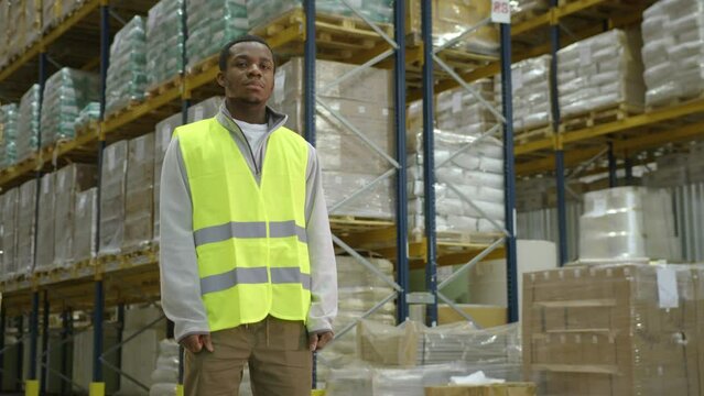 African American worker standing against racks with goods in industrial warehouse