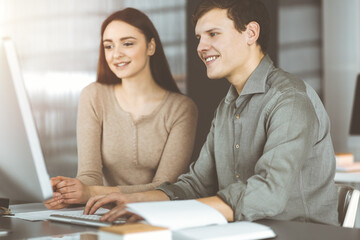 Handsome young businessman is looking at camera with a smile, while sitting together with female colleague in sunny office