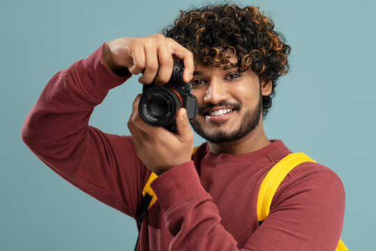 Young smiling Indian photographer holding photo camera taking pictures  isolated on gray background. Portrait of happy attractive asian tourist with backpack looking at camera. Travel concept 