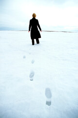 Rear view of woman in winter leaving footprints behind in snow.
