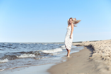 Happy blonde beautiful woman having fun on ocean beach while dancing in waves