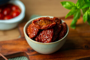 Bowl of sun dried tomatoes on wooden background.Dried tomato. Sun dried tomatoes. Infinite depth of field. Sun dried tomatoes with fresh herbs and spices. Slate background.Autumn seasonal pickled 