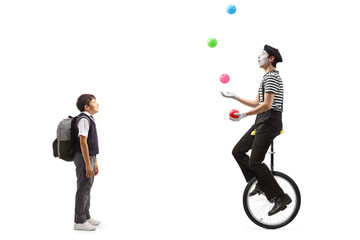 Full length shot of a schoolboy looking at a mime juggling and riding a unicycle