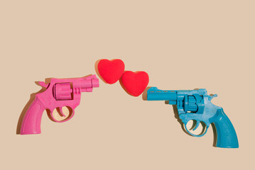 Creative valentines or romantic concept with pink and blue gun firing hearts on  yellow background. Minimal love concept.