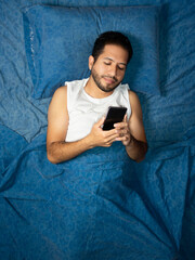 latin man using cell phone on blue bed, cell phone concept