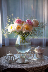 Still life with a bouquet of flowers, white and pink peonies, gypsophila in a vase on a table by the window, a cup, bicycle decor. Blur, selective focus