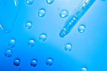 Naklejka na ściany i meble Water bubbles with cosmetic liquid drops of serum on a blue background of a laboratory glass pipette. Close-up of a pipette.