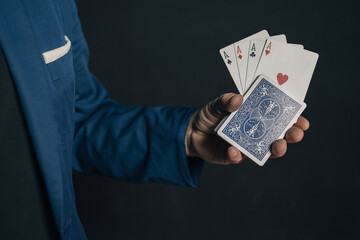 Close-up image of a young magician's hand in the dark holding a deck of cards and from it come the 4 aces of the French deck lined up.