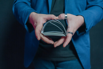 Close-up image of a young magician in the dark holding a deck of cards with both hands and putting them together and intermingling them with each other.