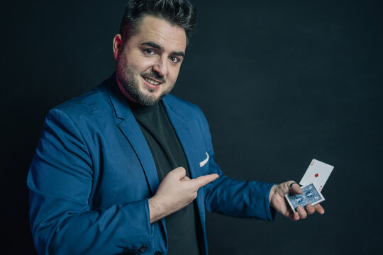 Portrait of a young magician in the dark pointing to a card he has taken out of the deck he is holding.