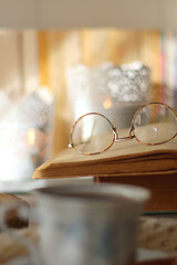 Vintage books, reading glasses, e-reader, cup of tea, bowl of biscuits and lit candle on the table. Selective focus.