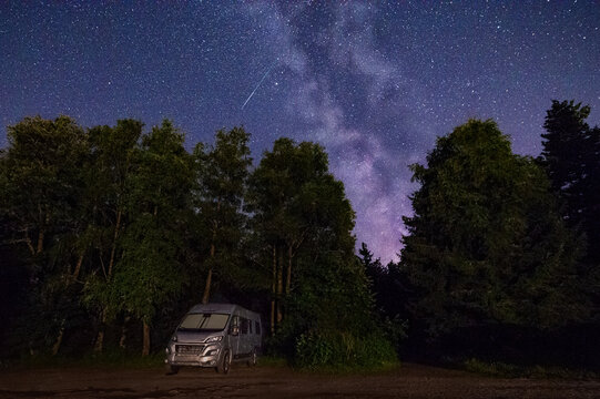 Wohnmobil nachts unter der Milchstra&szlig;e mit Sternschnuppe im Wald