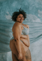 portrait of a plus size afro indigenous person standing with hand on heart smiling at camera
