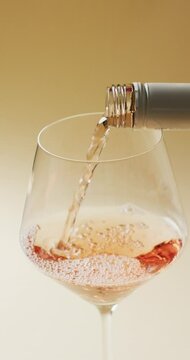 Vertical video of rose wine pouring from bottle into large wine glass