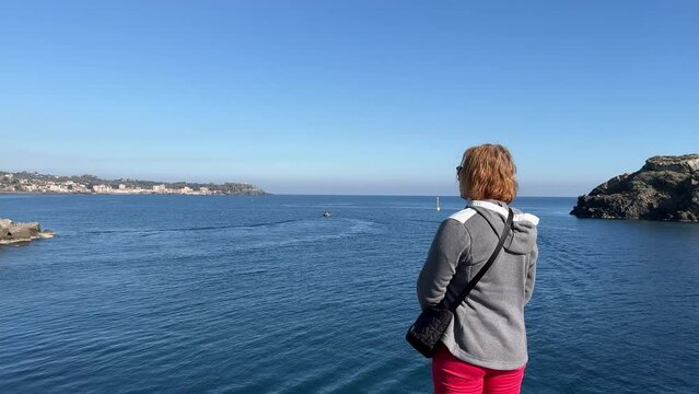 Tourist woman takes pictures with a smartphone of the sea and volcano. Woman looking at the sea and volcano Etna in Sicily, Acitrezza