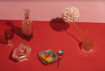 Red table for a party. Gummy candy, crystal bottle and glasses, teaspoon, pink flower and other things on the table..