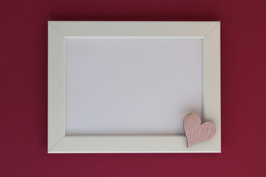 White frame on a burgundy background with a pink heart in the corner, with place for text