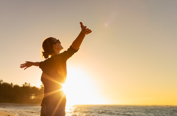 Young woman facing ocean sunset  rejoices, laughs, smiles looking up to the sky, enjoys life and...