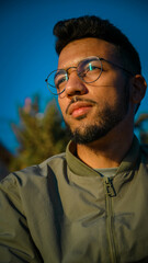 Hombre sentado al aire libre pensativo, con gafas y cielo azul