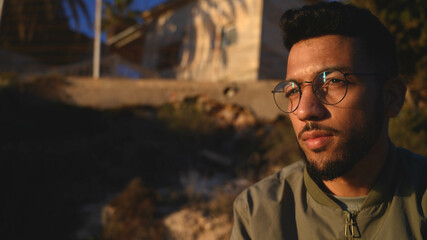 Hombre sentado al aire libre pensativo, con gafas y cielo azul