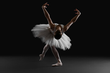 Young ballerina practicing dance moves on black background © New Africa