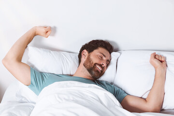 Happy man stretching on comfortable pillows in bed at home