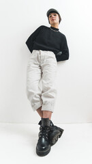 Modern fashion modeling. Fashionable woman in her 20s posing and leaning over white wall. Low angle. Vertical indoor shot. Copy space. Studio shot. High quality photo