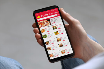 Food delivery service. Man choosing dish from menu on site using smartphone on light grey background, closeup