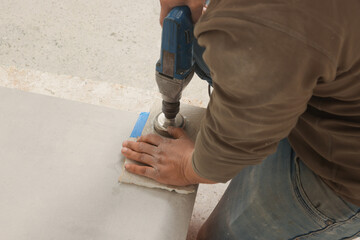 Worker with electric drill preparing tiles for installation indoors, closeup