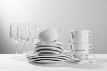 Set of clean dishware and glasses on white wooden table against light background
