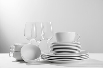 Set of clean dishware and glasses on white wooden table against light background