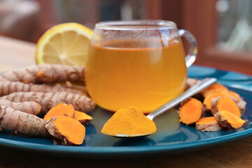 Plate with glass cup of hot tea, lemon, turmeric powder and roots on table