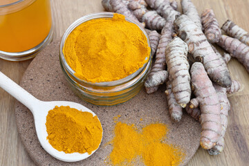 Glass jar of turmeric powder and roots on wooden table