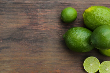 Whole and cut fresh ripe limes on wooden table, flat lay. Space for text