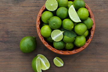 Whole and cut fresh ripe limes in bowl on wooden table, flat lay