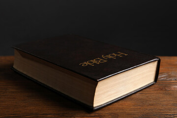 Hardcover Bible on wooden table against black background