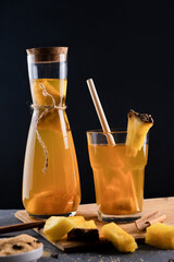 Pineapple Tepache. Fermented drink from pineapple served in glass and bottle in low key. Dark background.