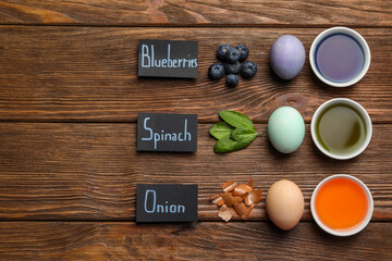Easter eggs painted with natural organic dyes, labels and space for text on wooden table, flat lay. Blueberries, spinach, onion used for coloring