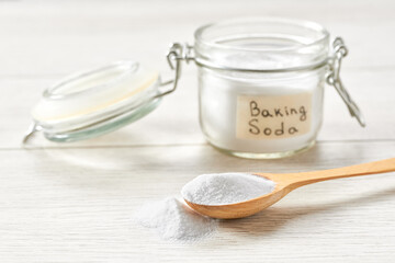Jar of baking soda on a light wooden table. Environmentally friendly detergent - baking soda on a white wooden table.