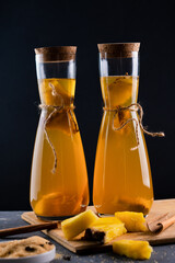 Pineapple Tepache. Fermented drink from pineapple served in bottles in low key. Dark background.