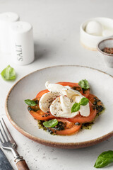 Caprese salad in modern feed with tomatoes, basil, mozzarella, pesto. Traditional Italian food with cutlery on white background with text space for menu