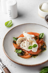 Caprese salad in modern feed with tomatoes, basil, mozzarella, pesto. Traditional Italian food with cutlery on white background, menu