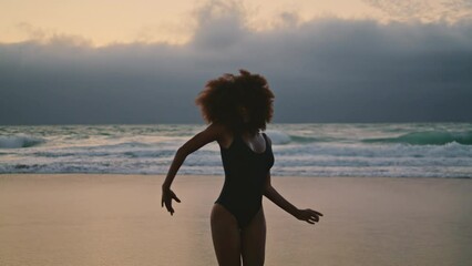 Silhouette woman performing belly dance on sand beach at overcast evening. 