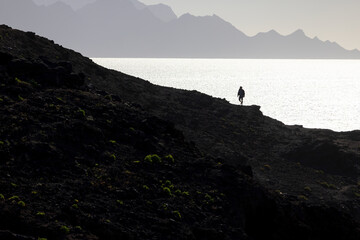 Along the Edge: A Man's Journey Across a Cliff with Ocean and Mountains as a Backdrop