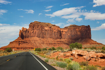 Highway leading to huge, red, sandstone monoliths - Road trip through the desert in Monument Valley in Utah