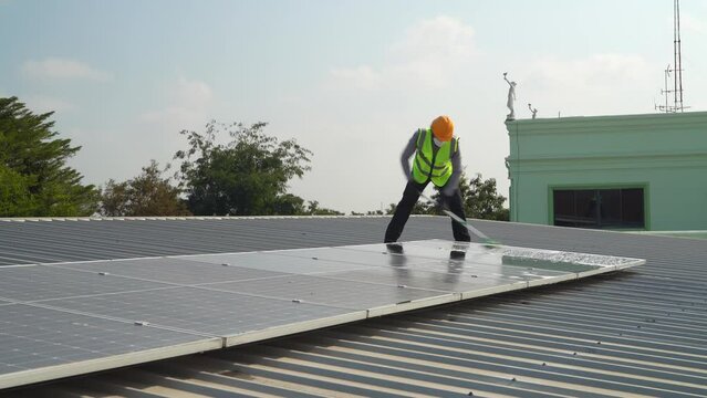 Maintenance technician using cleaning mop and to clean the solar panels that are dirty with dust to improve the efficiency of solar energy storage.